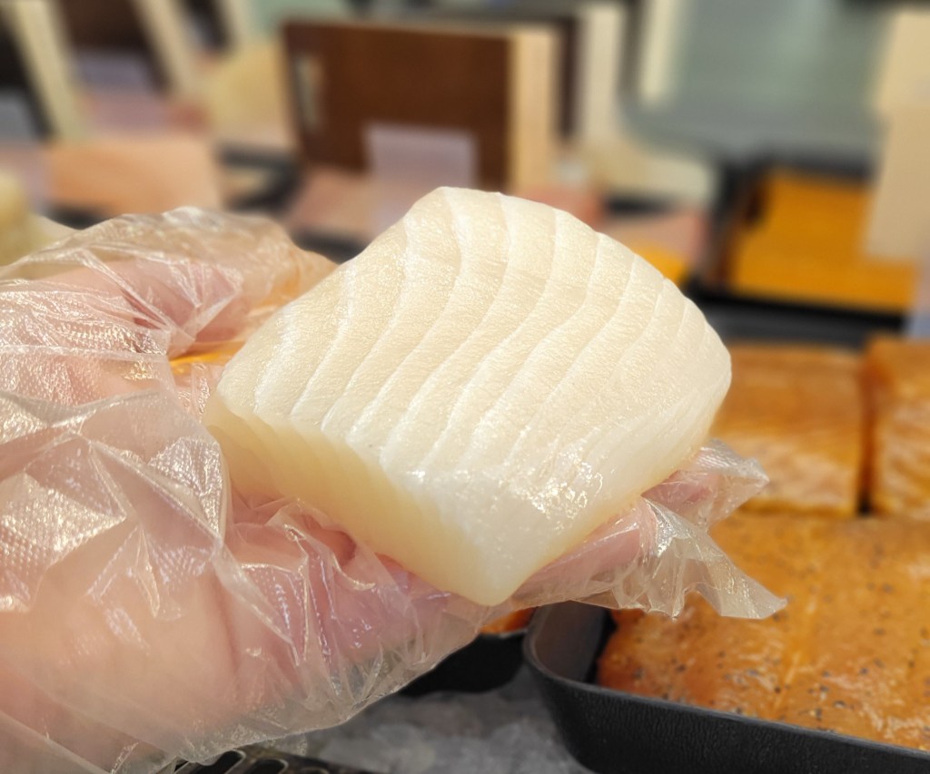 A close up of a person's plastic-gloved hand holding a thick square fillet of halibut, around 5 ounces.