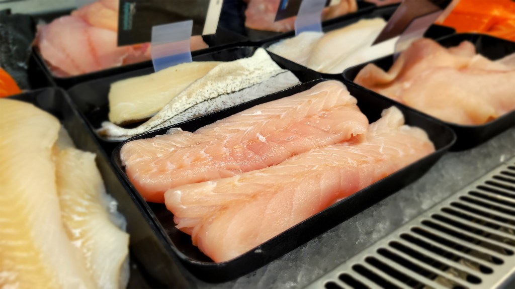Corvina fillets sit in a tray surrounded by other fish varieties in a traditional seafood display case.