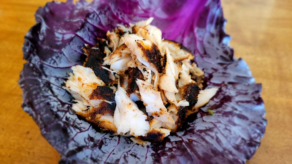 Blackened chunks of corvina piled in a red cabbage leaf. 